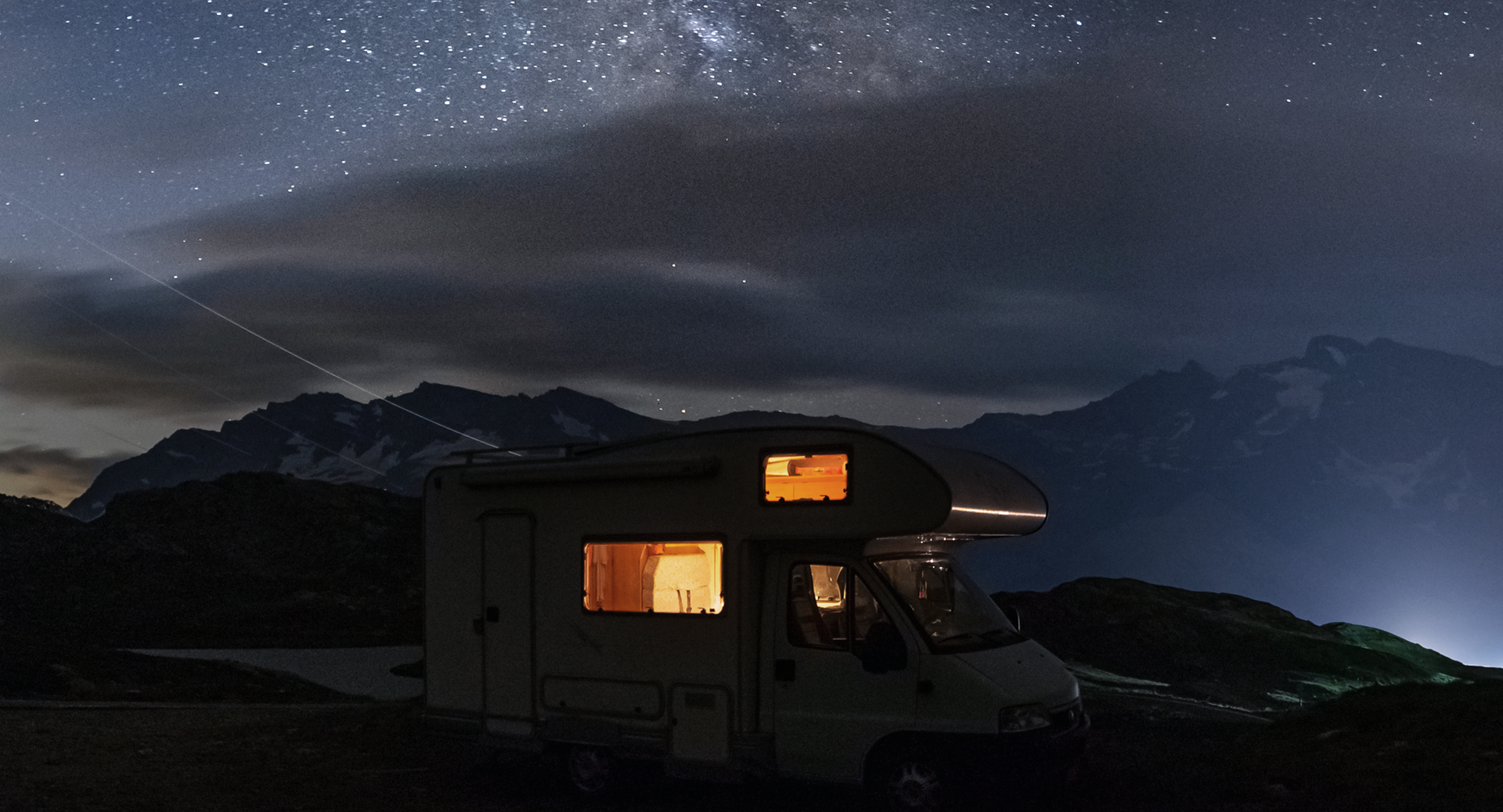 Wohnmobil vor einer Bergkulisse in der Nacht.