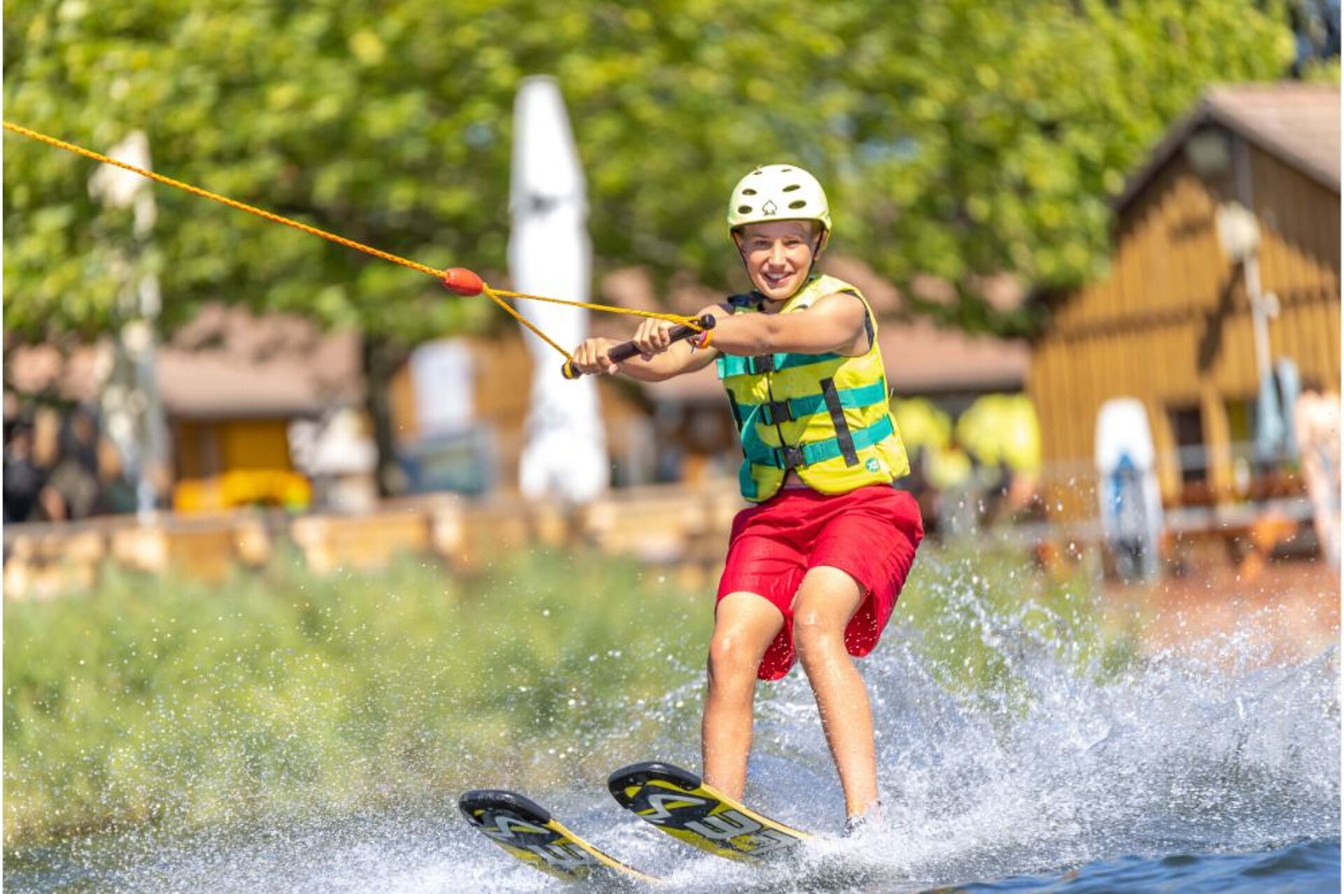 Ein Junge steht auf Skiern auf dem Wasser und hält sich an einer Leine fest