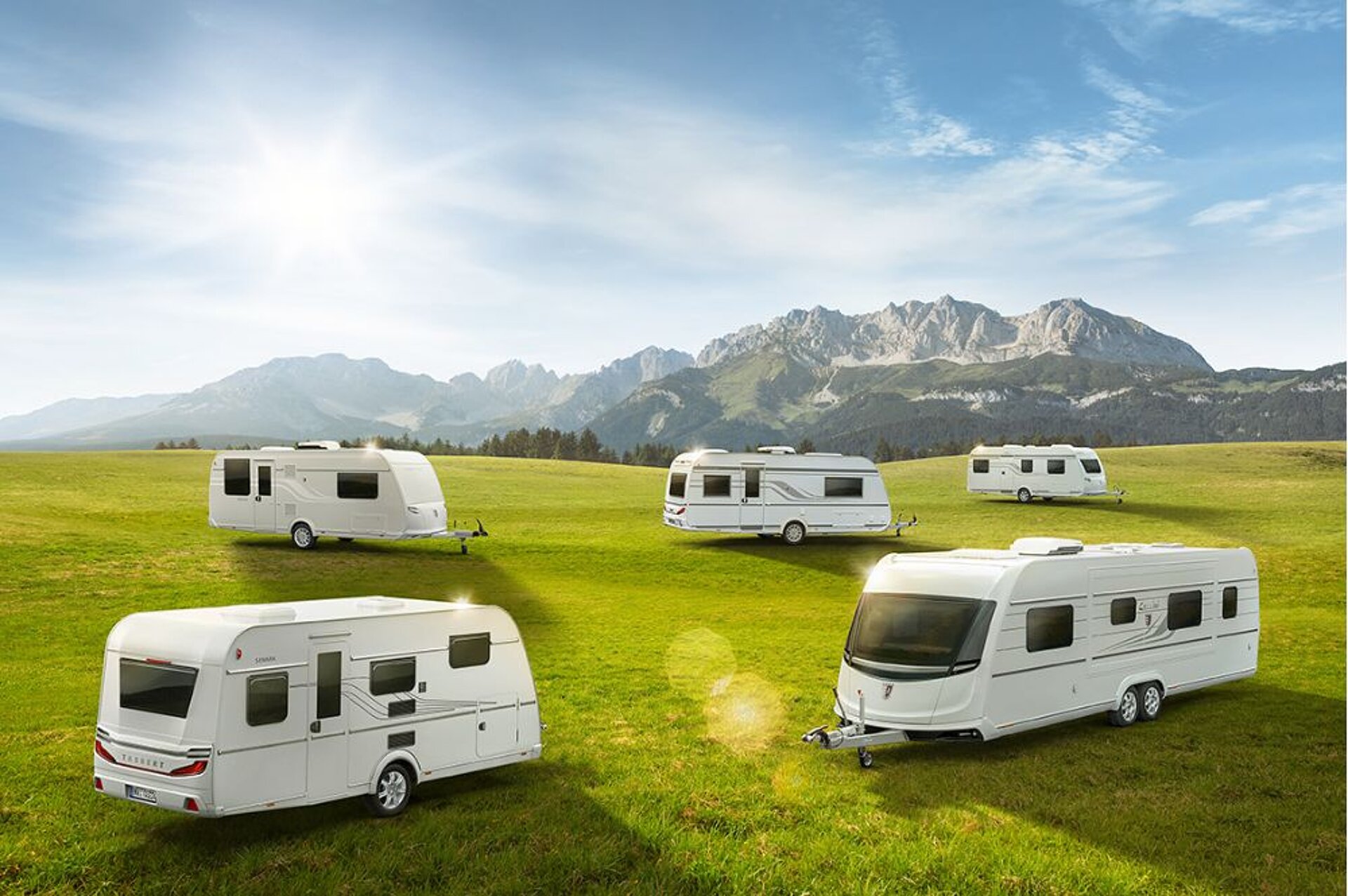 Fünf Wohnwagen stehen auf einer Wiese vor einem Bergpanorama