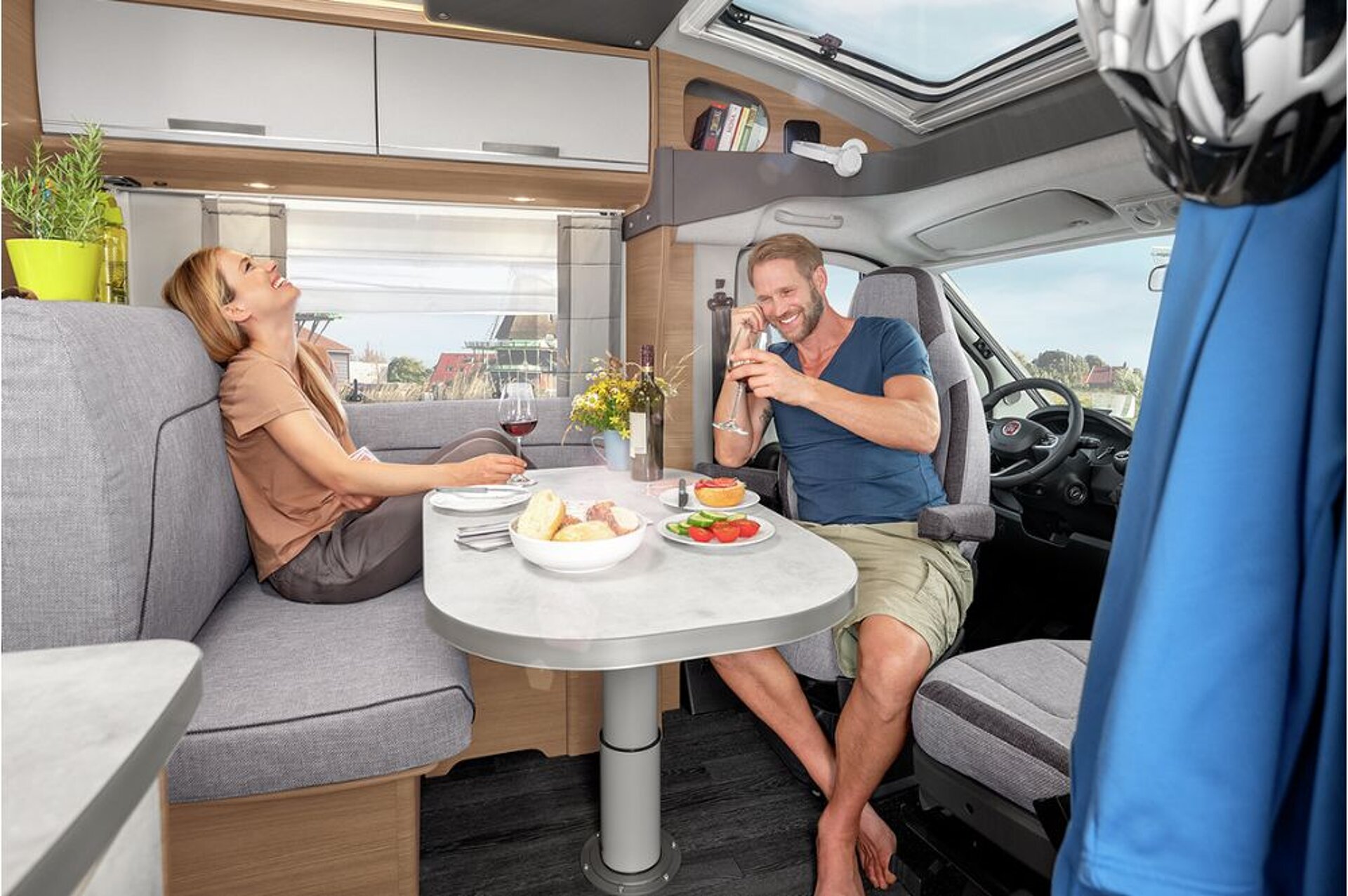 Ein Paar sitzt im Innenraum eines Reisemobils an dem gedeckten Tisch mit Wein und Brot.