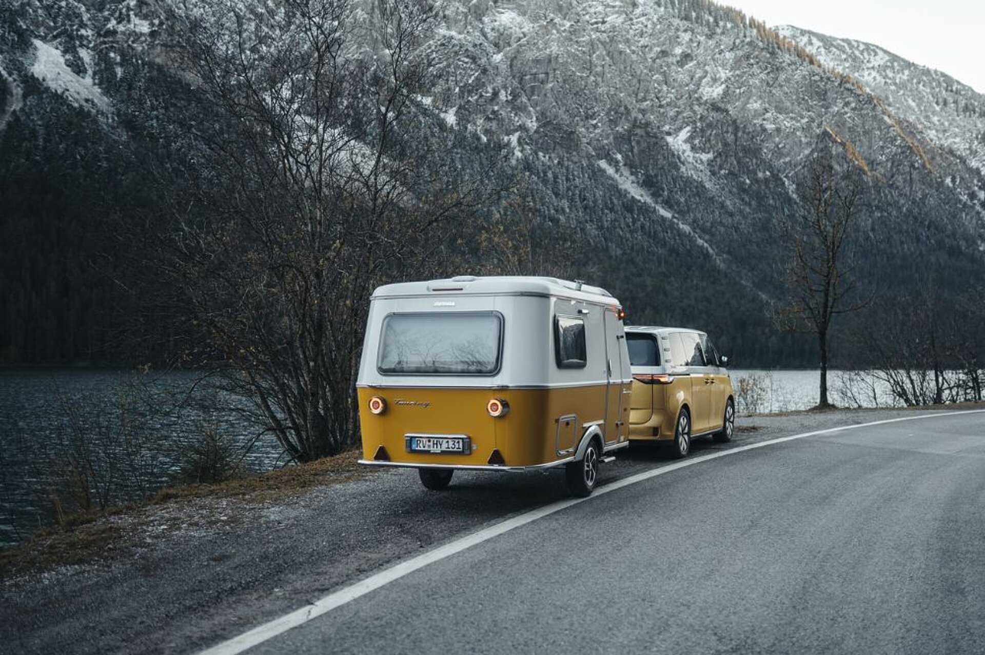 Ein Wohnwagen steht mit einem Bus vorne dran auf dem Seitenstreifen einer Straße am Wasser.