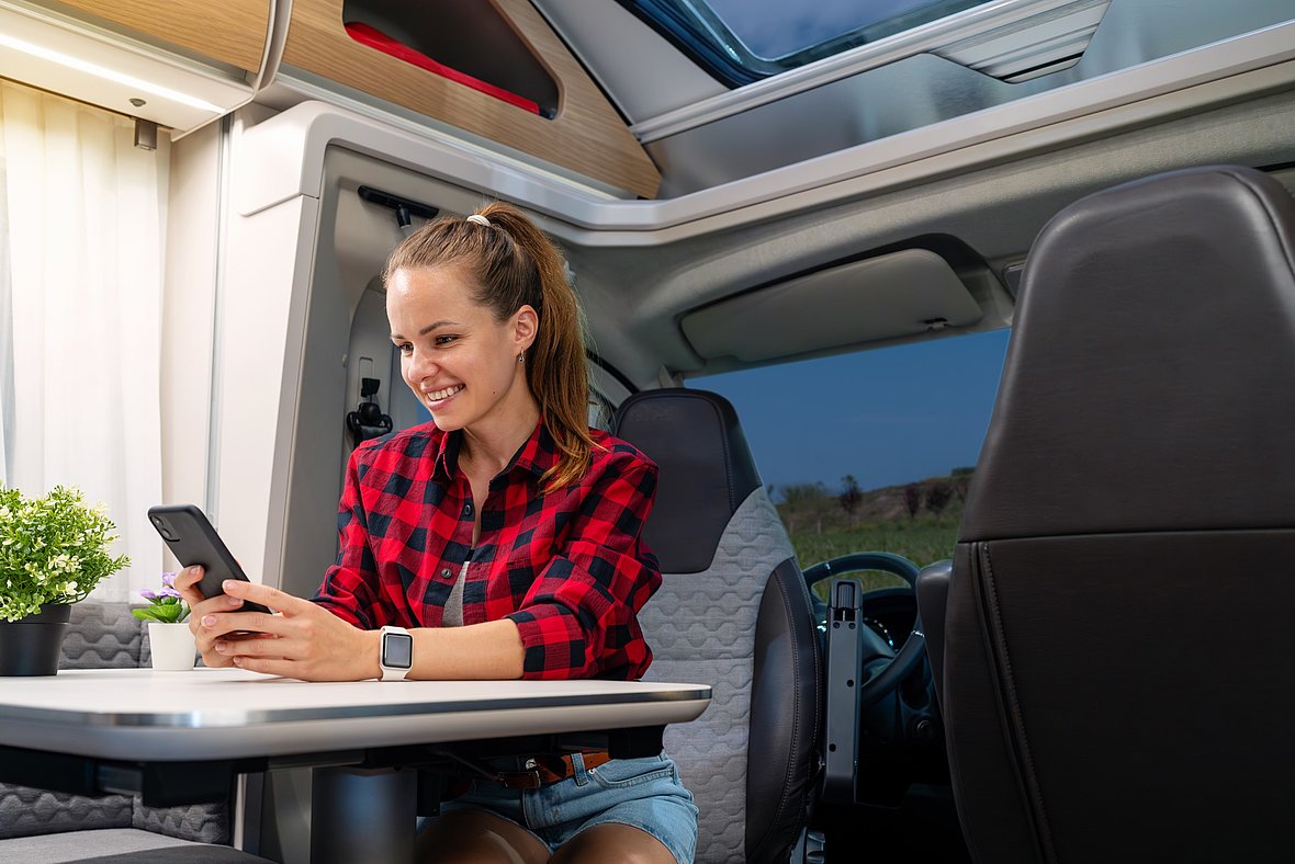 Eine junge Frau steuert die Technologie in ihrem Wohnmobil zentral über ihr Smartphone.