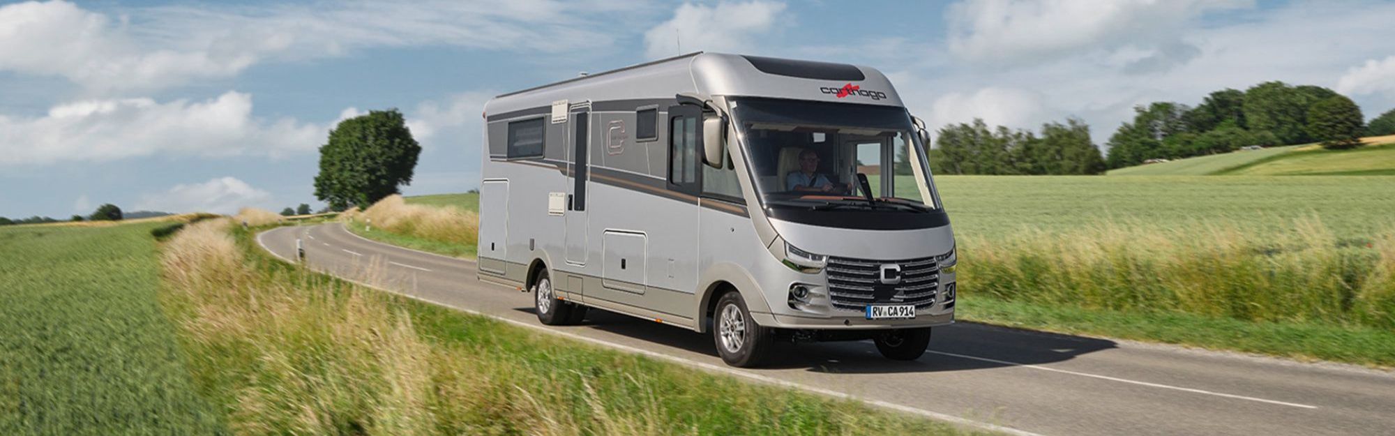 Ein Reisemobil fährt auf einer Straße zwischen zwei Wiesen entlang