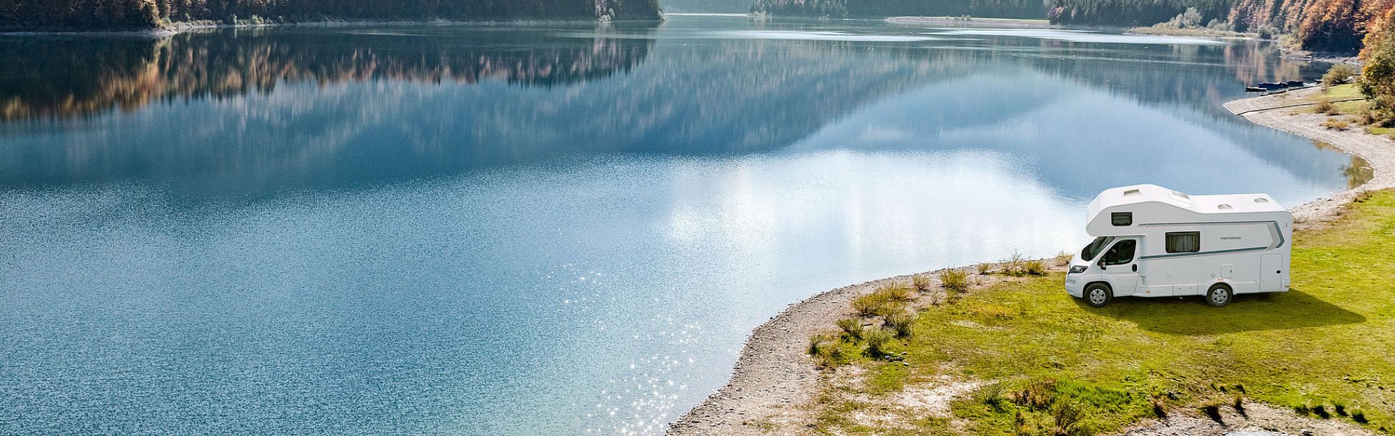 Ein Wohnmobil mit Alkoven steht auf einer Wiese an einem See
